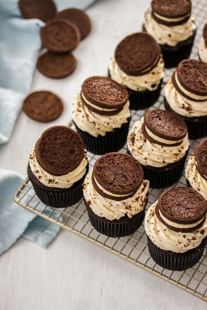 A batch of chocolate cupcakes with white frosting and a cookie on top of each. 