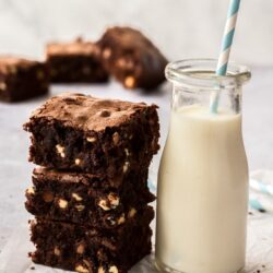 A stack of 3 chocolate chip brownies sitting next to a small bottle of milk