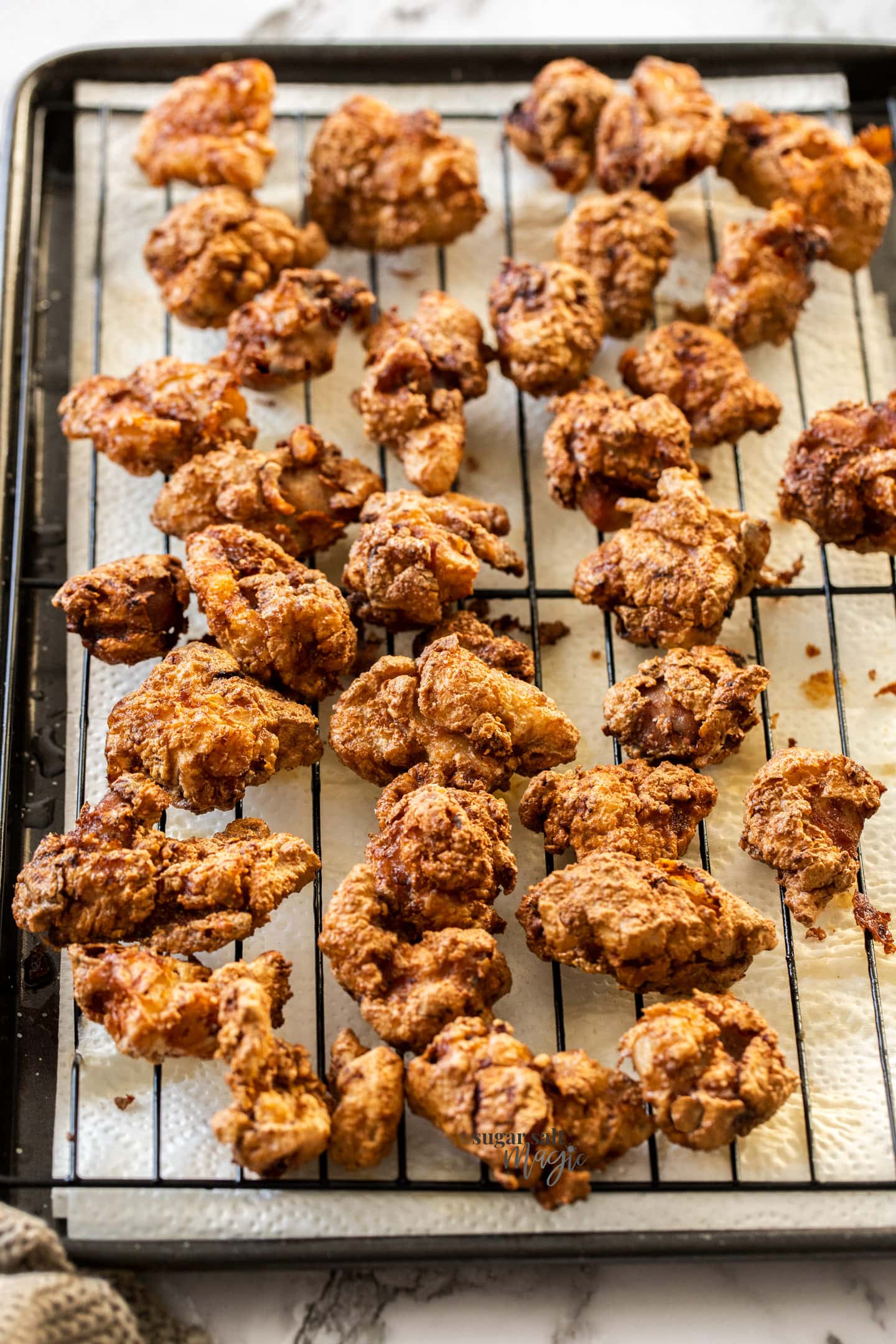 Small pieces of fried chicken on a rack over some paper towel.