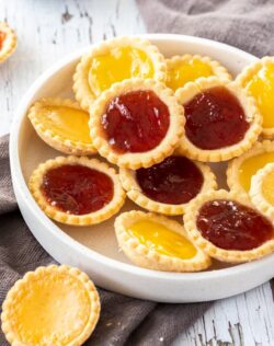 A white platter filled with jam tarts on a dark grey tea towel