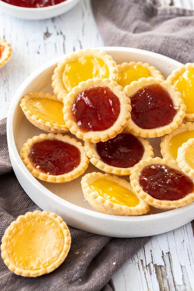A white platter filled with jam tarts on a dark grey tea towel