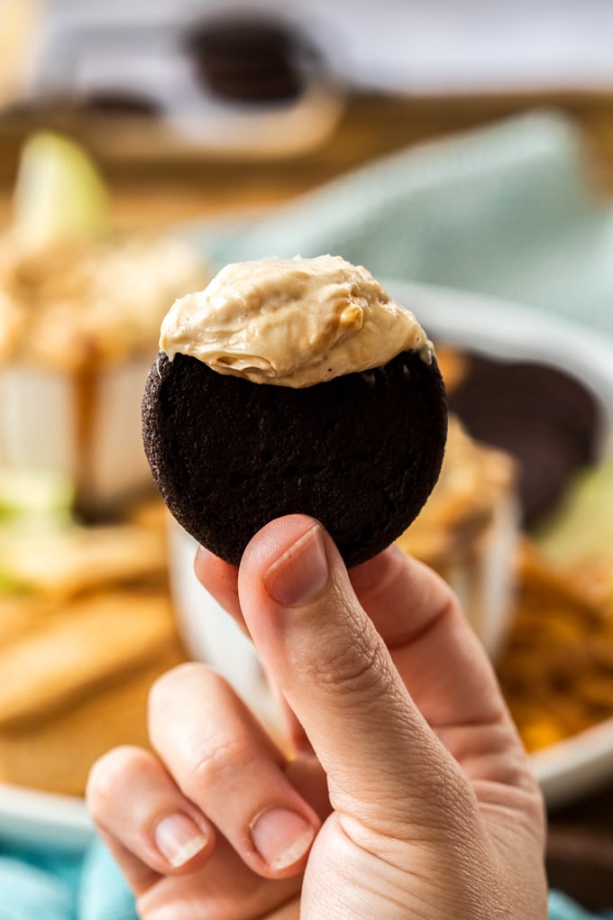 A hand holding up a very dark, almost black, cookie topped with cheesecake dip.