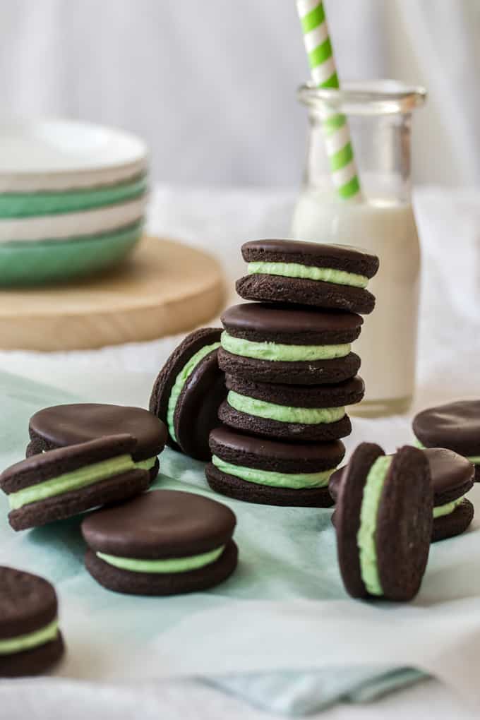 A stack of 4 dark chocolate biscuits filled with green buttercream with a bottle of milk in the background