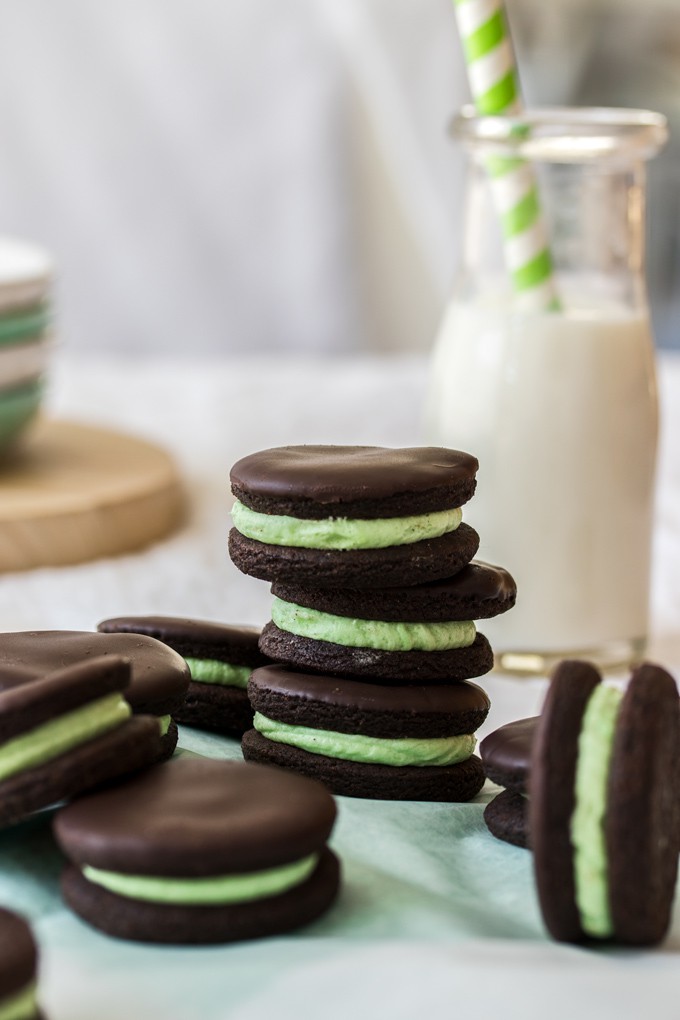 A stack of 3 chocolate cookies filled with green buttercream with a bottle of milk in the background