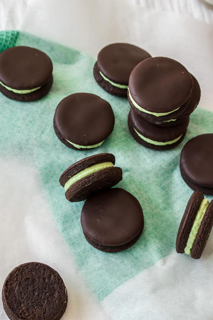 Chocolate cookies with green peppermint filling on a sheet of white baking paper on top of a green towel