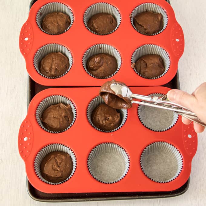 Portioning out chocolate cupcake batter into liners using a medium ice cream scoop.
