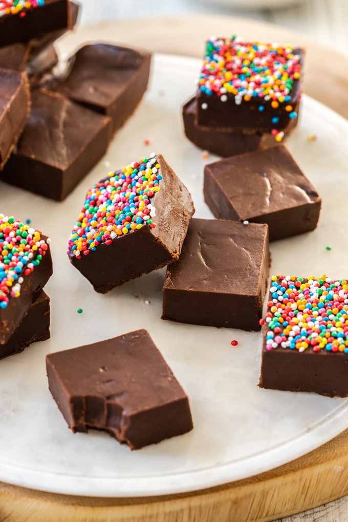 A batch of dark chocolate fudge pieces on a white marble platter. some have sprinkles on them