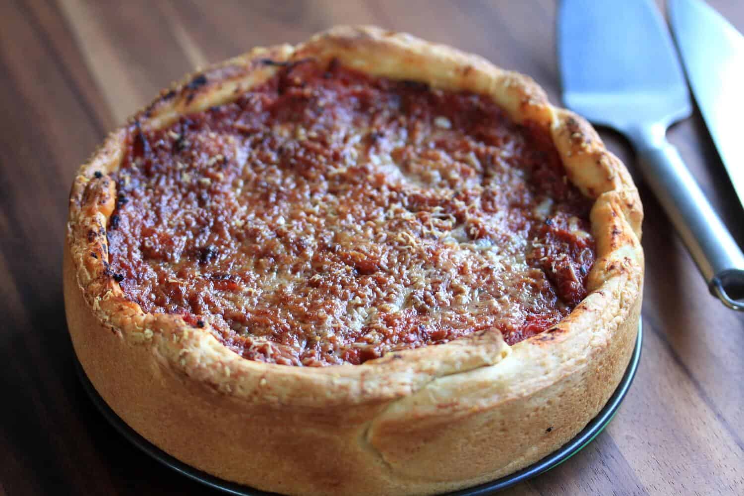 A whole Chicago deep dish pizza on a wooden board.