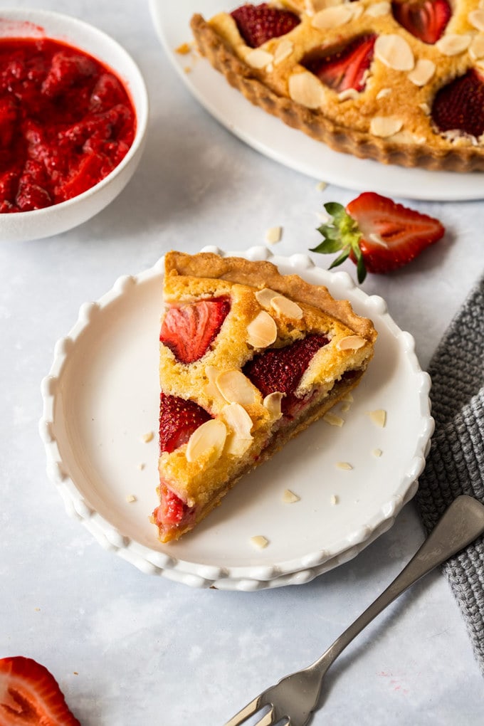 Birdseye view of a slice of strawberry tart on a white dessert plate with a dessert fork in front.