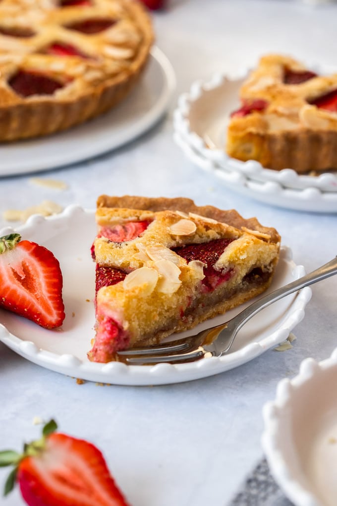 A slice of strawberry tart on a white plate with a fork sitting next to it. More slices in the background
