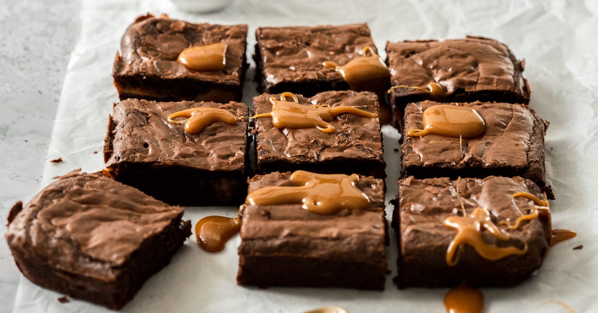 9 squares of Chocolate Caramel Brownies sitting on a piece of white baking paper