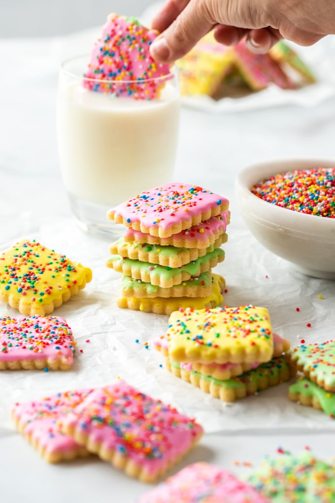 Different coloured iced cookies covered in sprinkles on a sheet of baking paper.