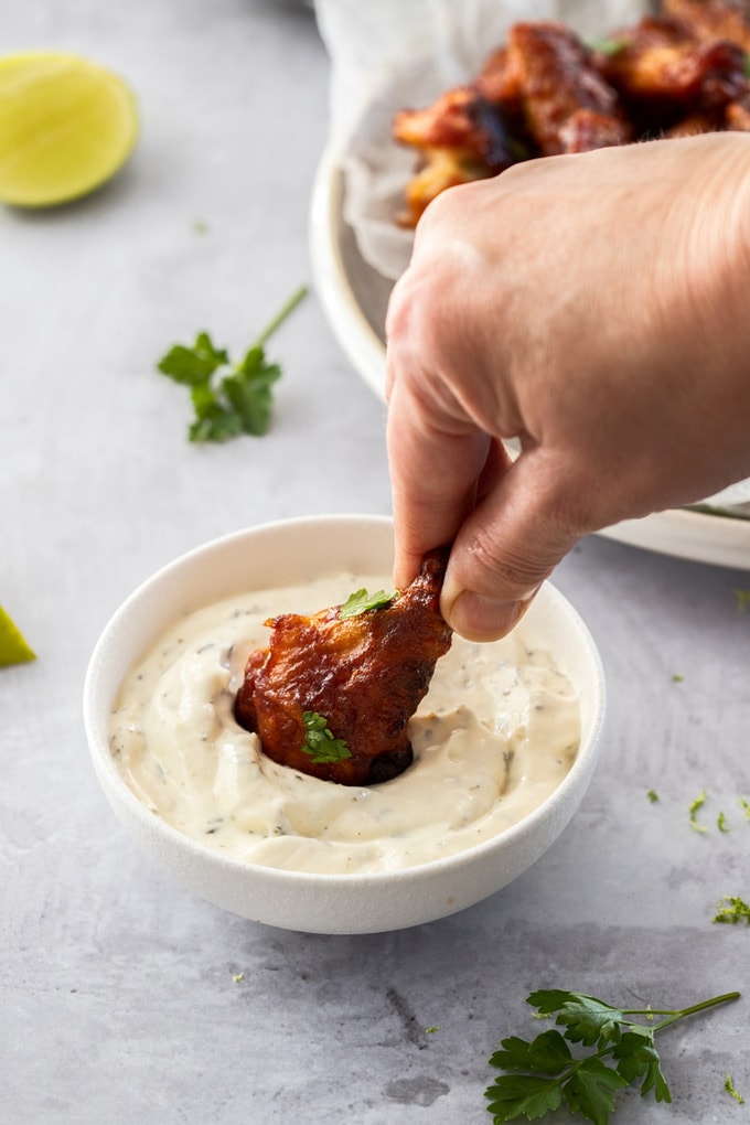 A chicken wing being dipped into a white bowl filled with ranch dip.