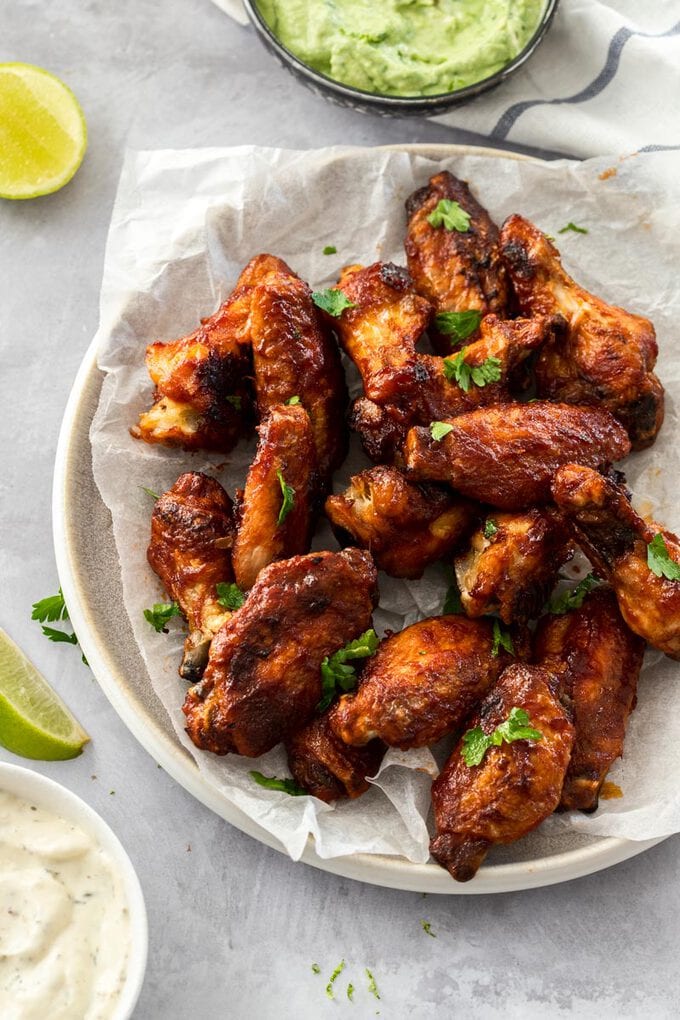 A plate of barbecue chicken wings with a bowl of ranch dip next to them.