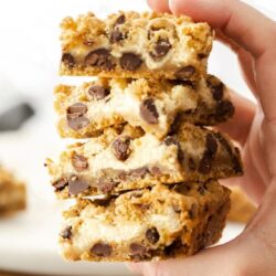 A hand holding 4 chocolate chip cheesecake bars