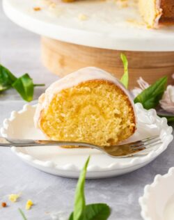 A slice of vanilla bundt cake with lemon curd filling on a small white cake plate with a fork sitting next to it.