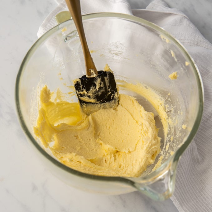 A glass mixing bowl with creamed butter and sugar on a marble surface