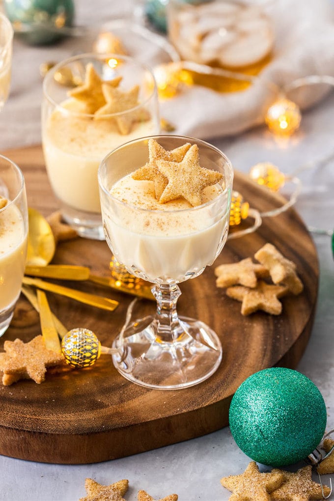 A goblet filled with eggnog panna cotta on a wooden board, surrounded by shortbread and festive ornaments