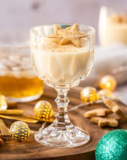 A goblet filled with eggnog panna cotta on a wooden board, surrounded by shortbread and festive ornaments