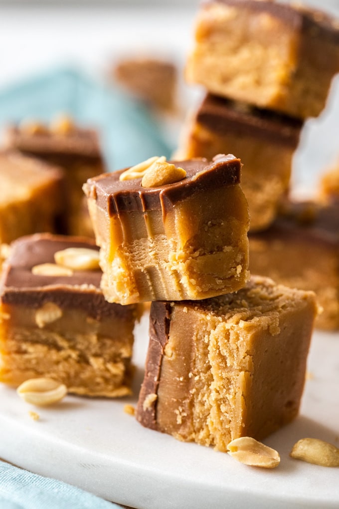 Pieces of caramel peanut fudge stacked up on a white platter. One with a bite taken out of it