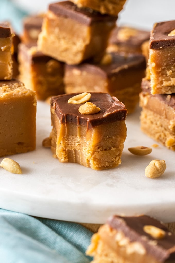 Pieces of caramel peanut fudge stacked up on a white platter. One with a bite taken out of it