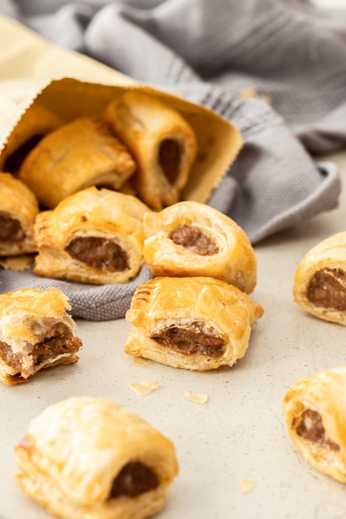 Mini homemade sausage rolls tumbling out of a browne paper bag.