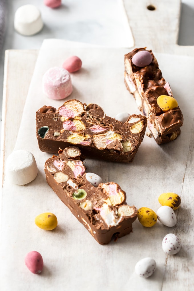 3 slices of rocky road on a white board, surrounded by marshmallows and easter eggs.