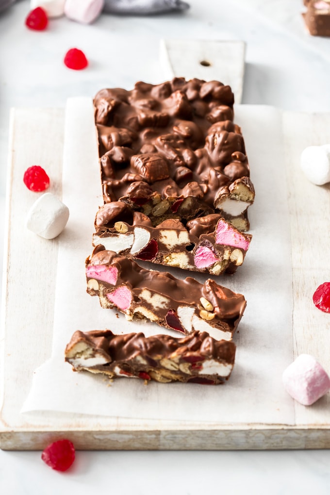 Rocky Road slices sitting on a white board, surrounded by marshmallows and candy.