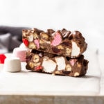 Two pieces of rocky road topped one on the other, surrounded by marshmallows on a white board