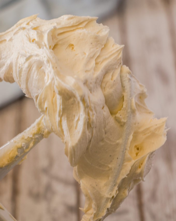 A closeup of whipped vanilla buttercream on a stand mixer paddle.