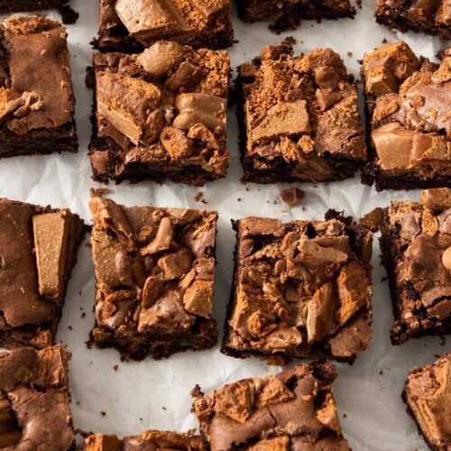 Top down view of a batch of 16 brownies on a sheet of white baking paper