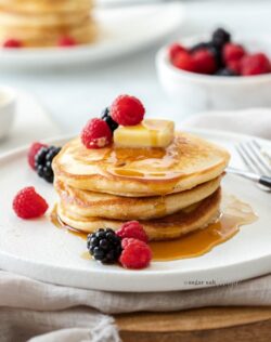 A stack of 3 pancakes on a white plate, topped with berries and butter