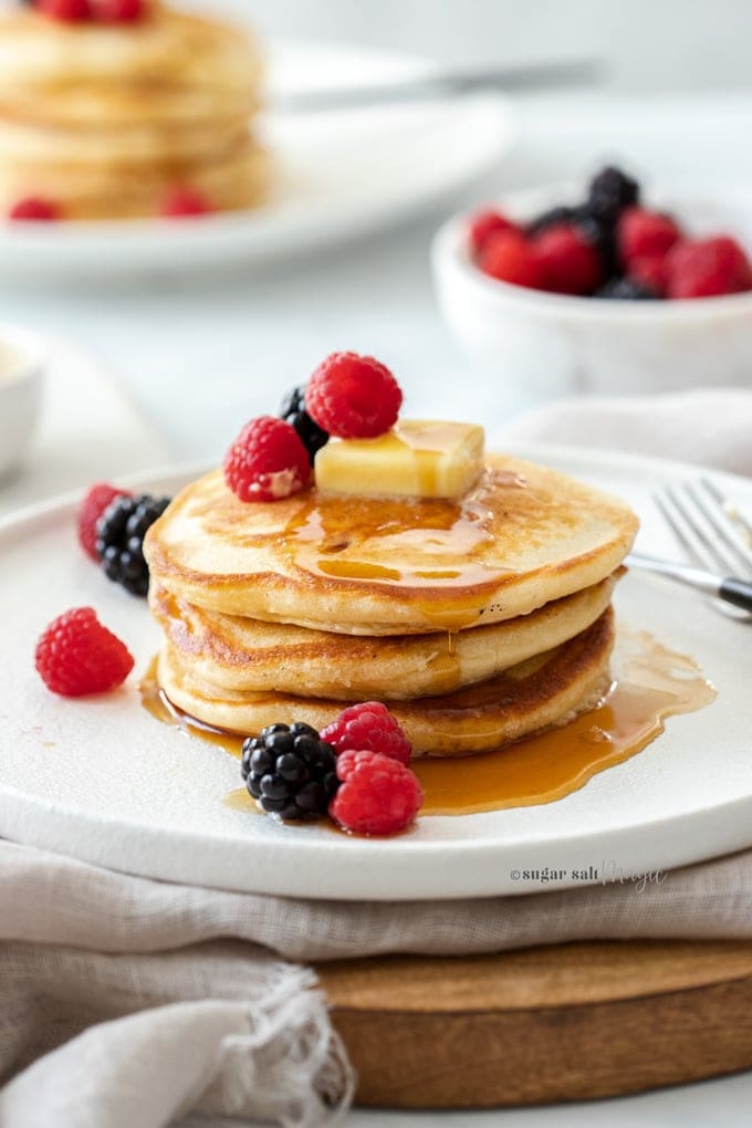 A stack of 3 pancakes on a white plate, topped with berries and butter