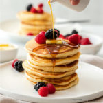 A stack of fluffy pancakes on a white plate surrounded by berries