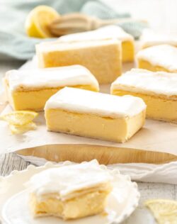 A batch of vanilla custard slice on a sheet of baking paper on a wooden board. Once sits on a plate in front with a bite taken out