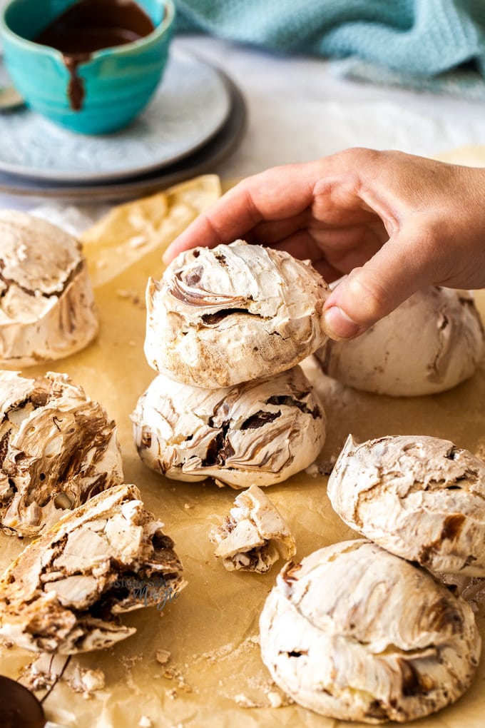 A batch of chocolate meringue on a sheet of baking paper and a hand reach to grab one.