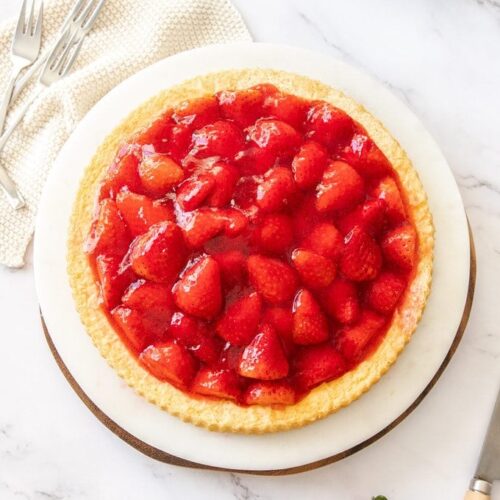 Top down view of a strawberry flan on a marble platter with strawberries scattered around