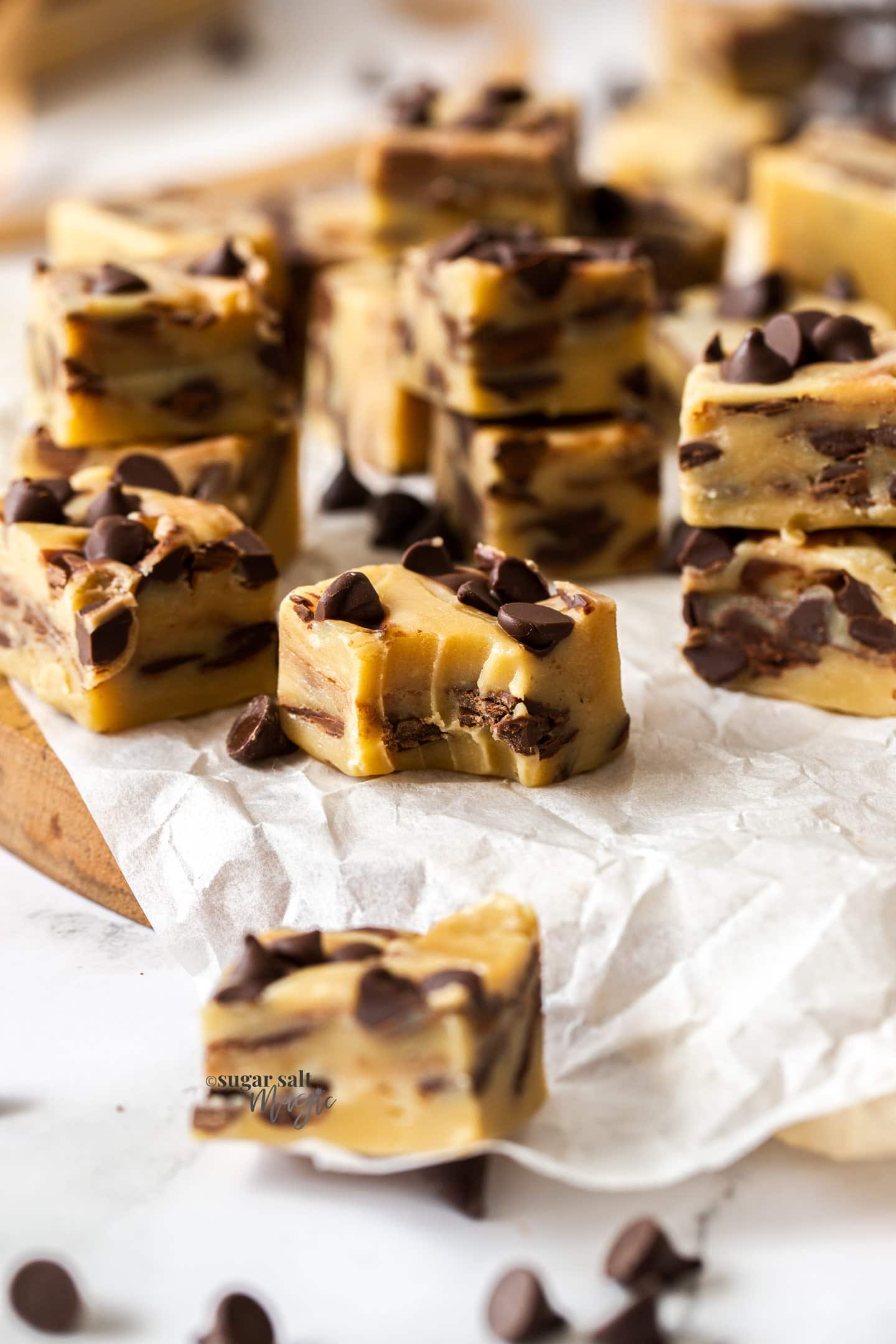 Squares of chocolate chip fudge on a sheet of baking paper. One with a bite taken out