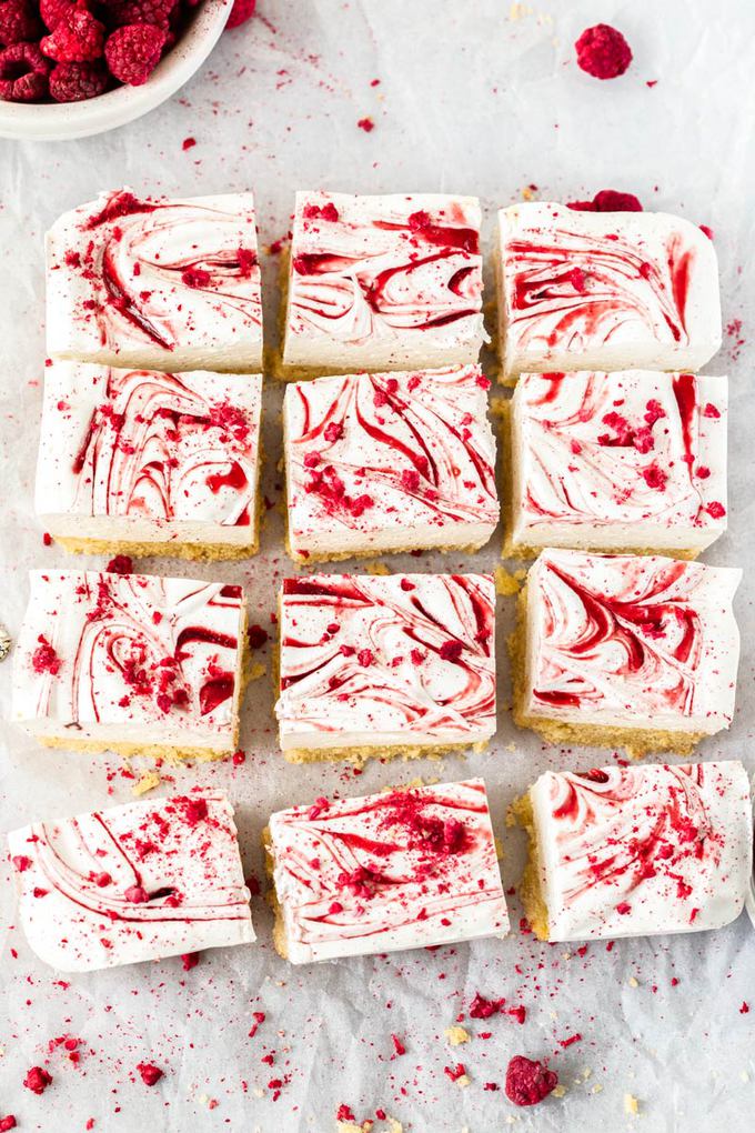 12 squares of marsmallow slice lined up on a crumpled piece of white baking paper. freeze dried raspberries scattered around