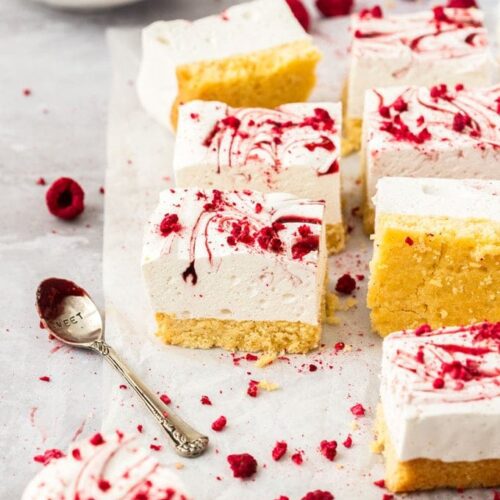 8 squares of marsmallow slice on a crumpled piece of white baking paper. freeze dried raspberries scattered around and a spoon covered in jam