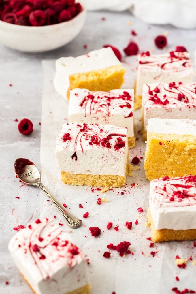 8 squares of marsmallow slice on a crumpled piece of white baking paper. freeze dried raspberries scattered around and a spoon covered in jam