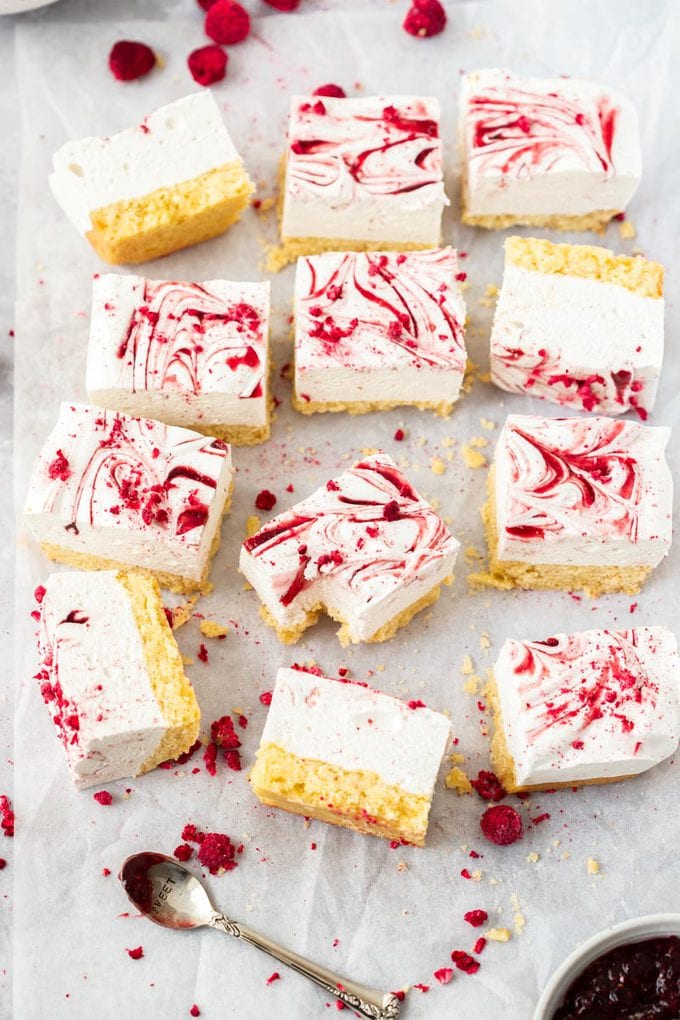 12 squares of marsmallow slice on a crumpled piece of white baking paper. freeze dried raspberries scattered around