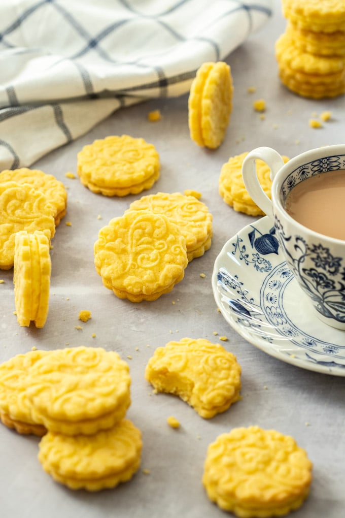 Custard creams laying on a gray surface in random positions next to a cup of tea