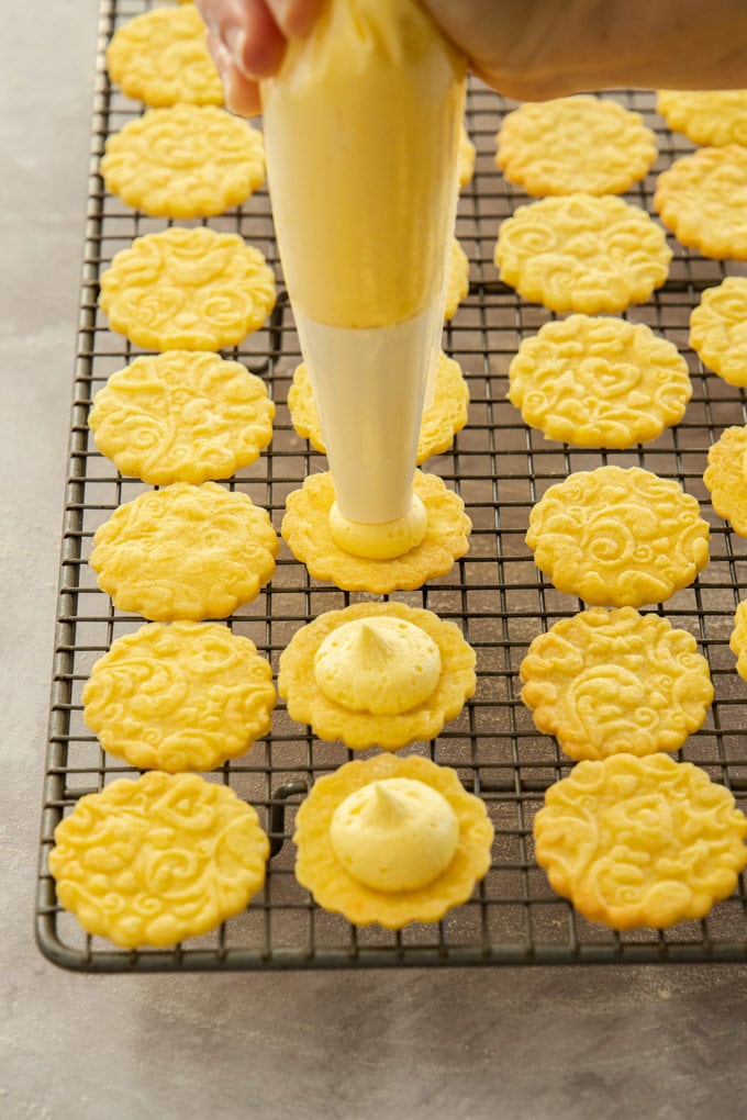 Cookies on a wire rack being filled with custard cream