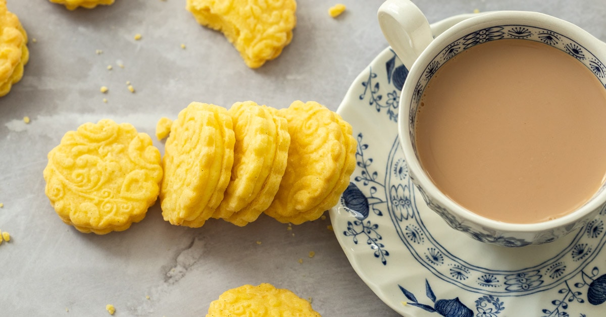 4 custard cream biscuits leaning up against a saucer. A cup of tea on top is filled with tea.