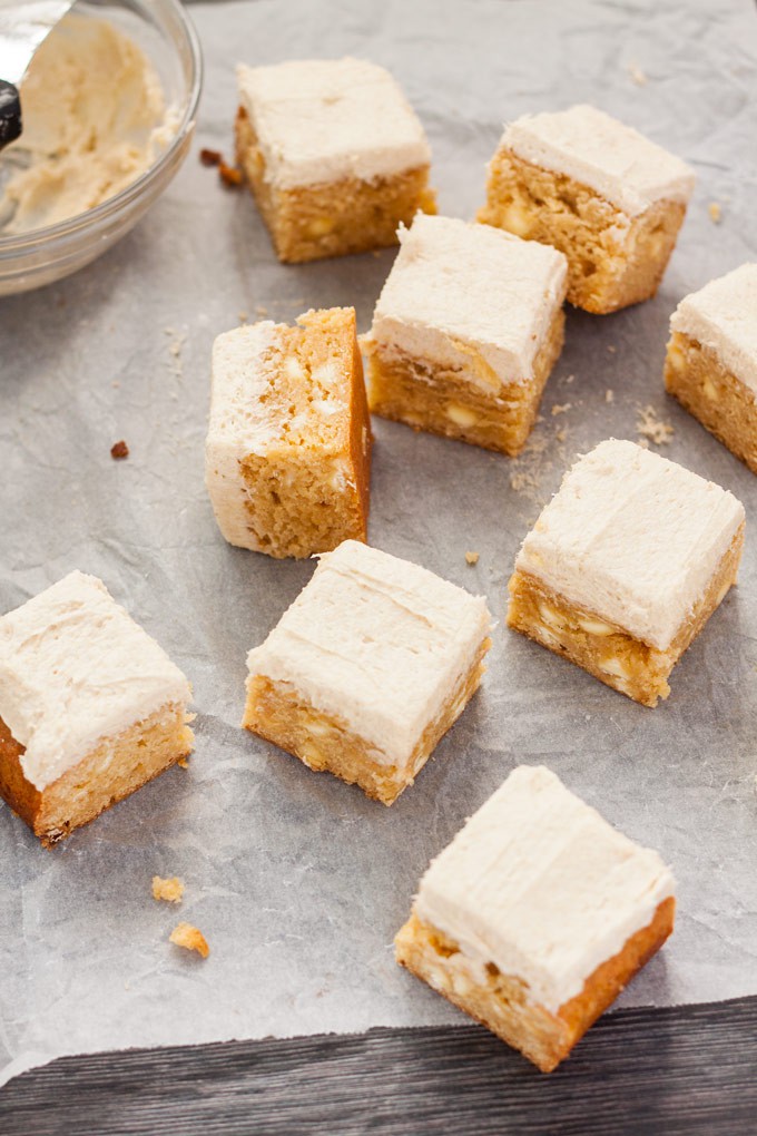 Top down view of a batch of blondies on a sheet of baking peper. They have frosting on top.