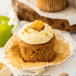 A closeup of an apple pie cupcake with the paper peeled away showing the texture of the cake. It sits on a marble worktop