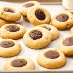 A batch of cookies with chocolate centres on a sheet of baking paper in a baking tin.