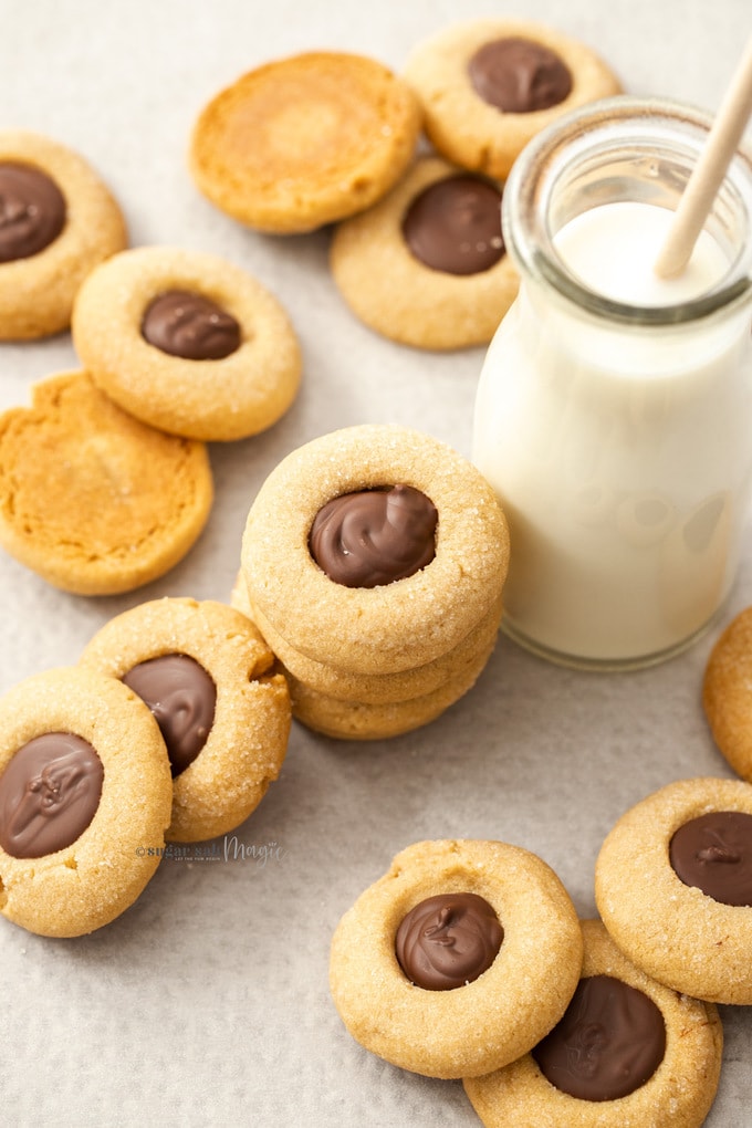 A batch of cookies with chocolate centres on a sheet of baking paper leaning up against a small bottle of milk