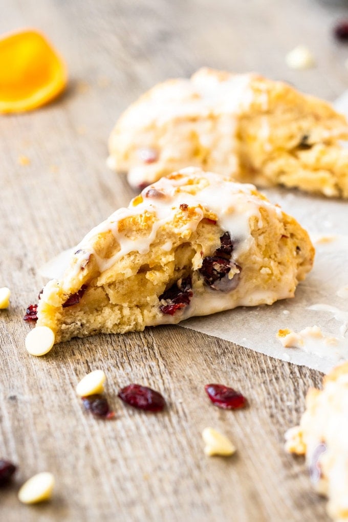 a cranberry scone on a wooden board with white chocolate chips and dried cranberries around it